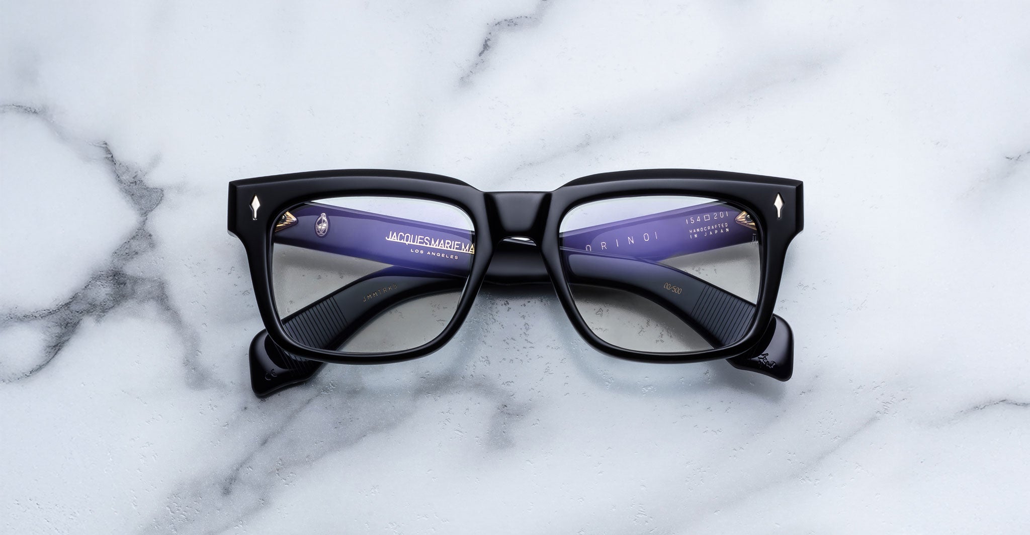 Jacques Marie Mage Torino black bold rectangular eyeglasses with clear lenses, by Jacques Marie Mage, are displayed on a white marble surface.