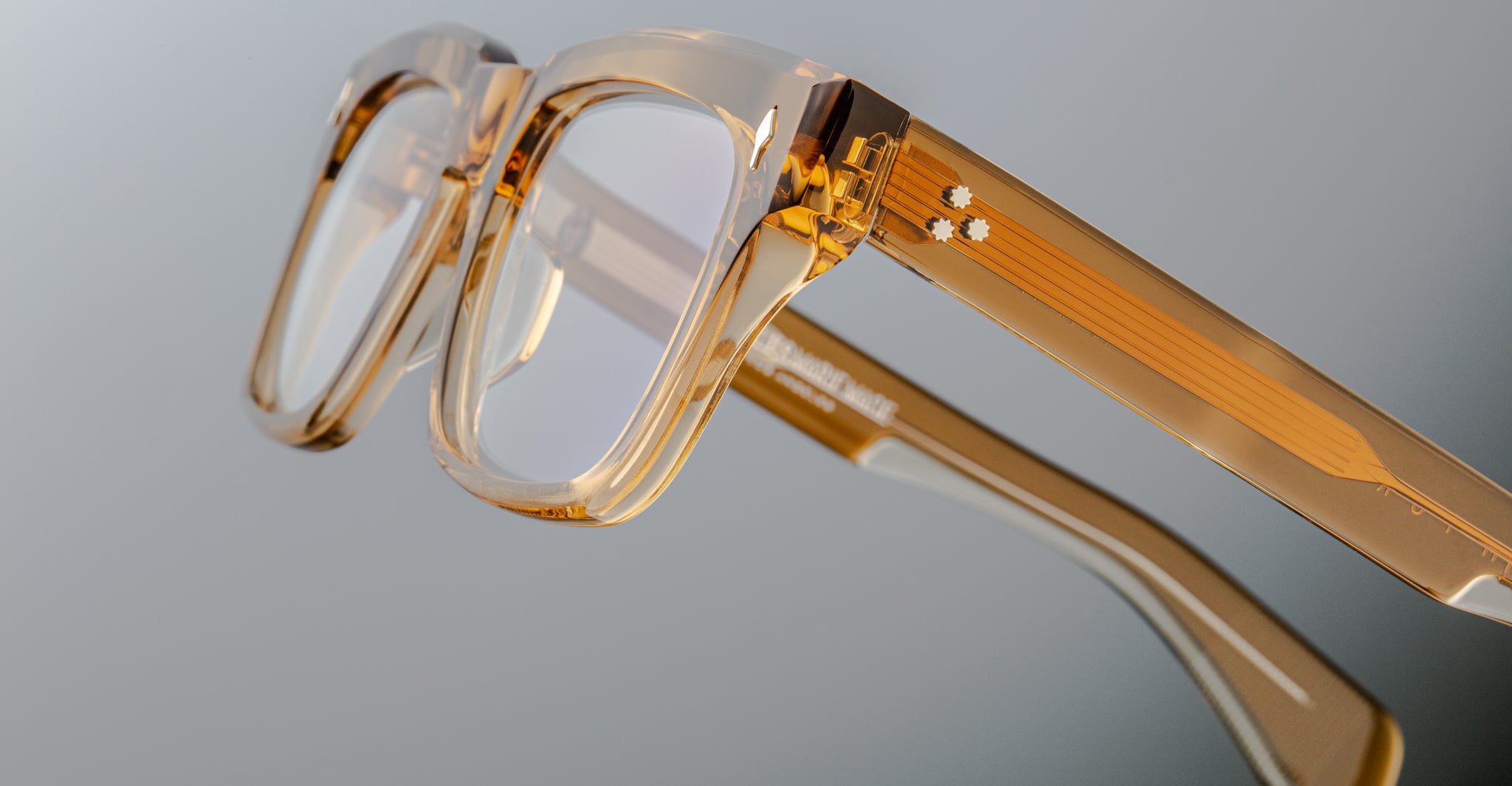 The Jacques Marie Mage Torino by Jacques Marie Mage is a thick, clear-framed rectangular eyeglass in translucent amber acetate, inspired by bold designs and shown close up against a neutral background.