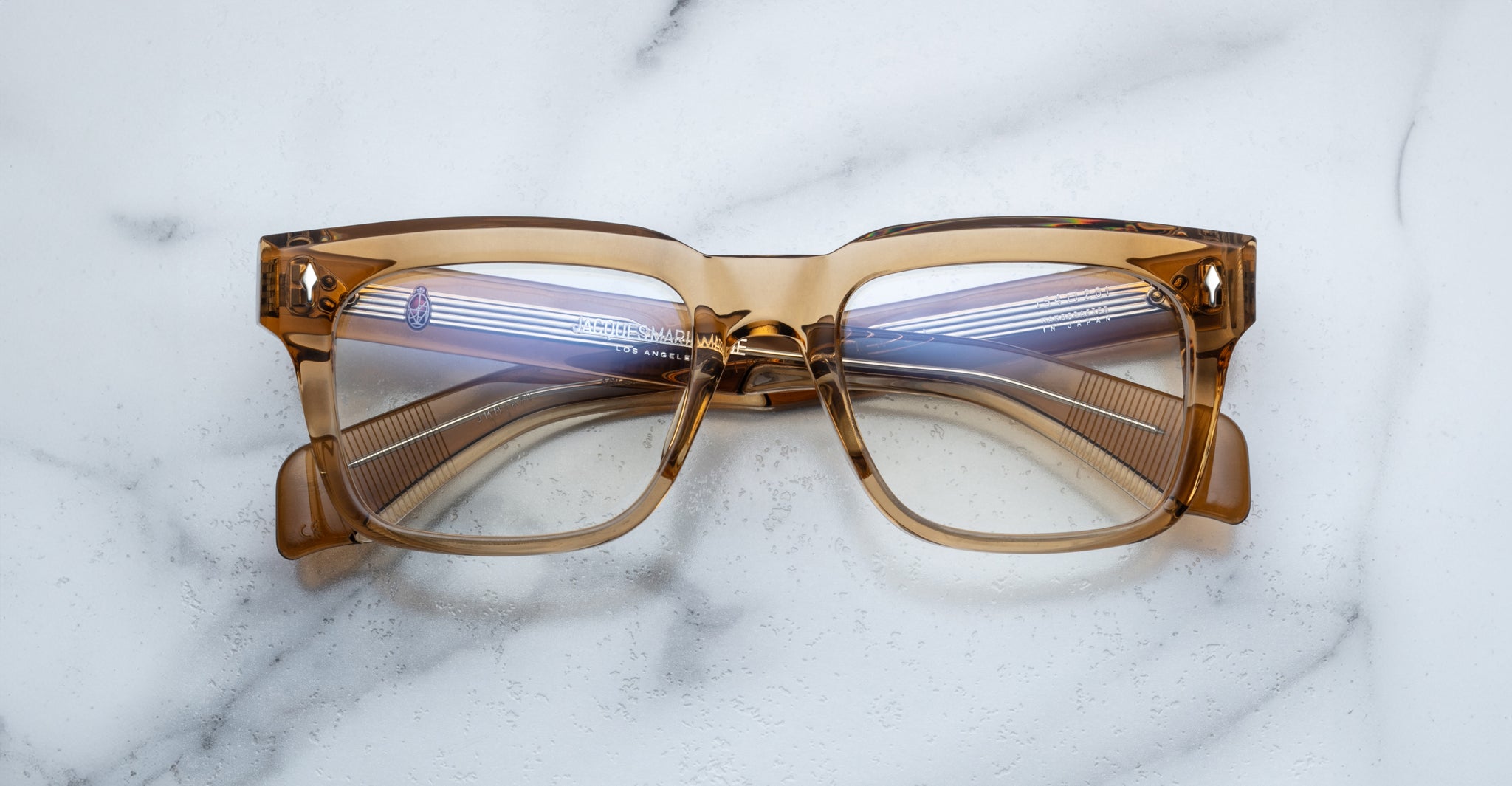 The Jacques Marie Mage Torino eyeglasses feature bold, handcrafted acetate rectangular frames with clear lenses, displayed on a white marble surface.