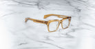 The Jacques Marie Mage Torino, bold rectangular eyeglass frames by Jacques Marie Mage, are crafted from translucent brown handcrafted acetate and displayed on a white marble surface.