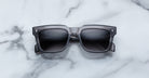 Jacques Marie Mage Torino sunglasses by Jacques Marie Mage, featuring bold rectangular black frames and dark lenses, displayed on a white marble surface.