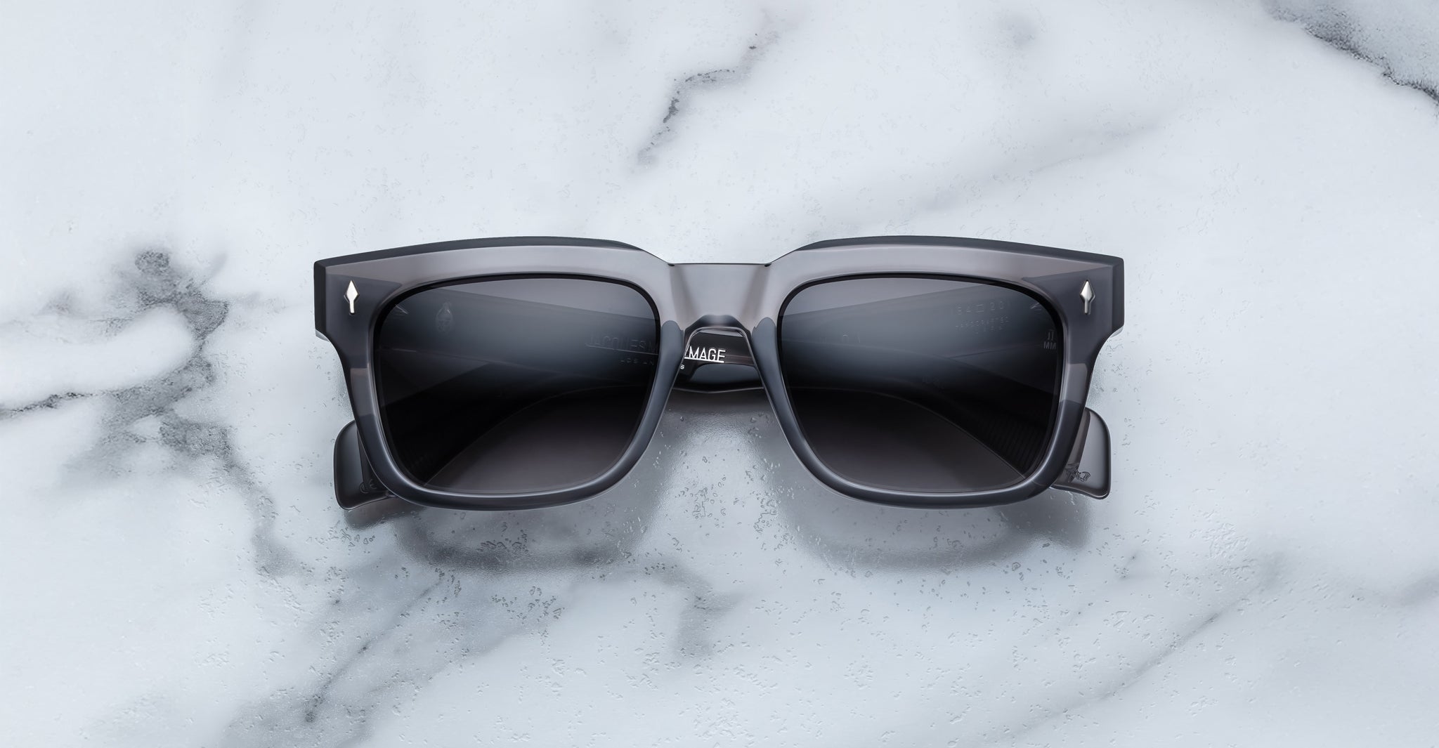 Jacques Marie Mage Torino sunglasses by Jacques Marie Mage, featuring bold rectangular black frames and dark lenses, displayed on a white marble surface.