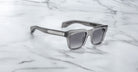 Jacques Marie Mage Torino rectangular sunglasses with dark lenses and bold handcrafted acetate frames rest on a white marble surface.