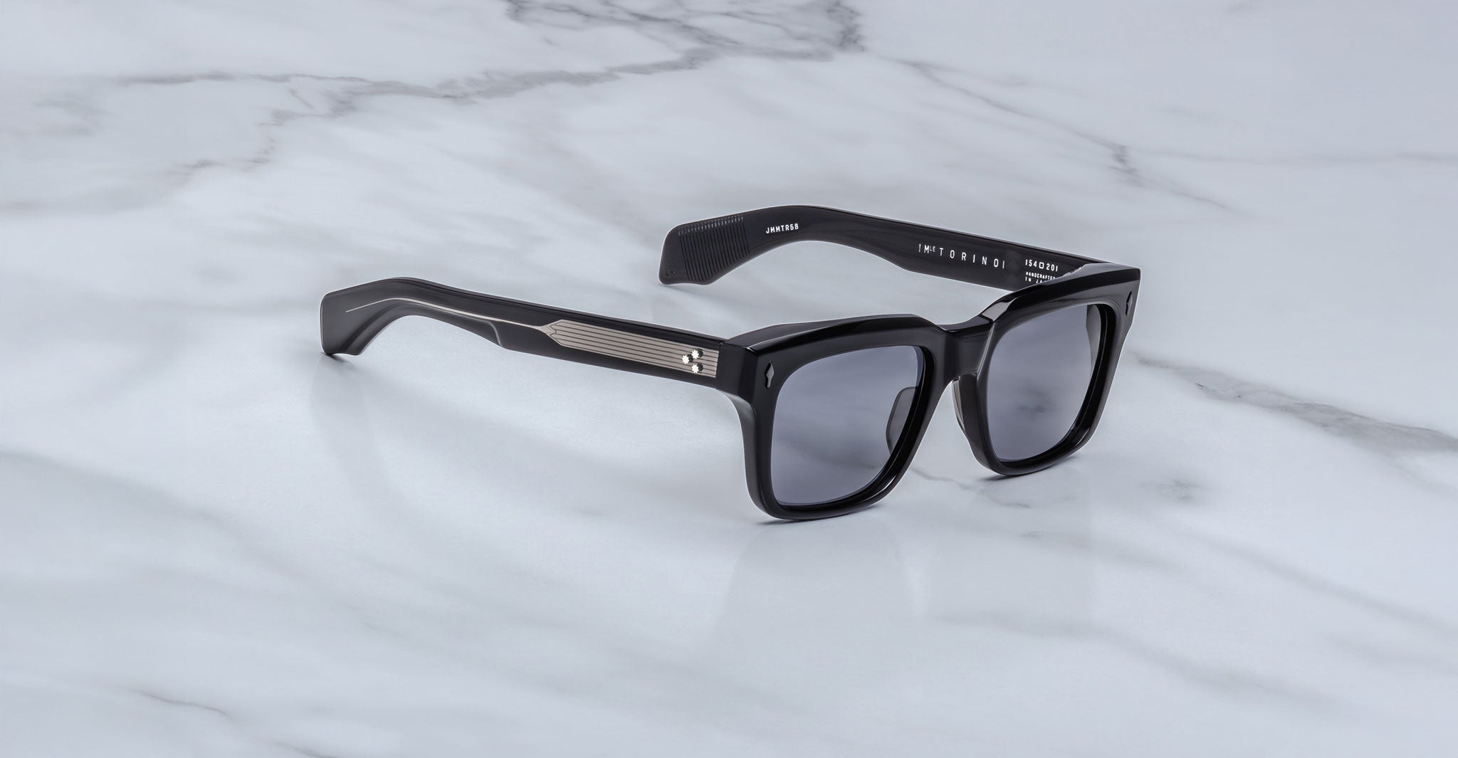 Showcasing the artistry of handcrafted acetate, Jacques Marie Mage Torino features bold black rectangular frames with dark lenses and metal temple accents, displayed on a white marble surface.
