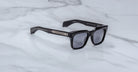 Showcasing the artistry of handcrafted acetate, Jacques Marie Mage Torino features bold black rectangular frames with dark lenses and metal temple accents, displayed on a white marble surface.