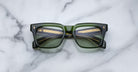 A pair of Jacques Marie Mage Torino rectangular eyeglass frames in bold green handcrafted acetate with dark lenses, inspired by the brand's signature style, displayed on a white marble surface.