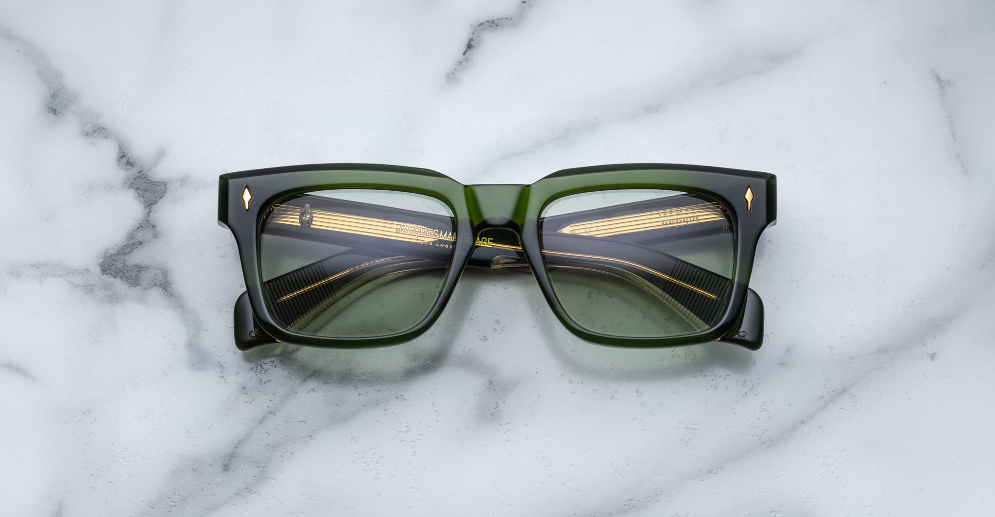A pair of Jacques Marie Mage Torino rectangular eyeglass frames in bold green handcrafted acetate with dark lenses, inspired by the brand's signature style, displayed on a white marble surface.
