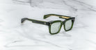 Jacques Marie Mage Torino sunglasses by Jacques Marie Mage, featuring a bold green rectangular design with gold accents, are displayed on a white marble surface.
