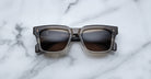 The Jacques Marie Mage Torino, bold rectangular eyeglass frames in dark brown handcrafted acetate by Jacques Marie Mage, rests on a white marble surface.
