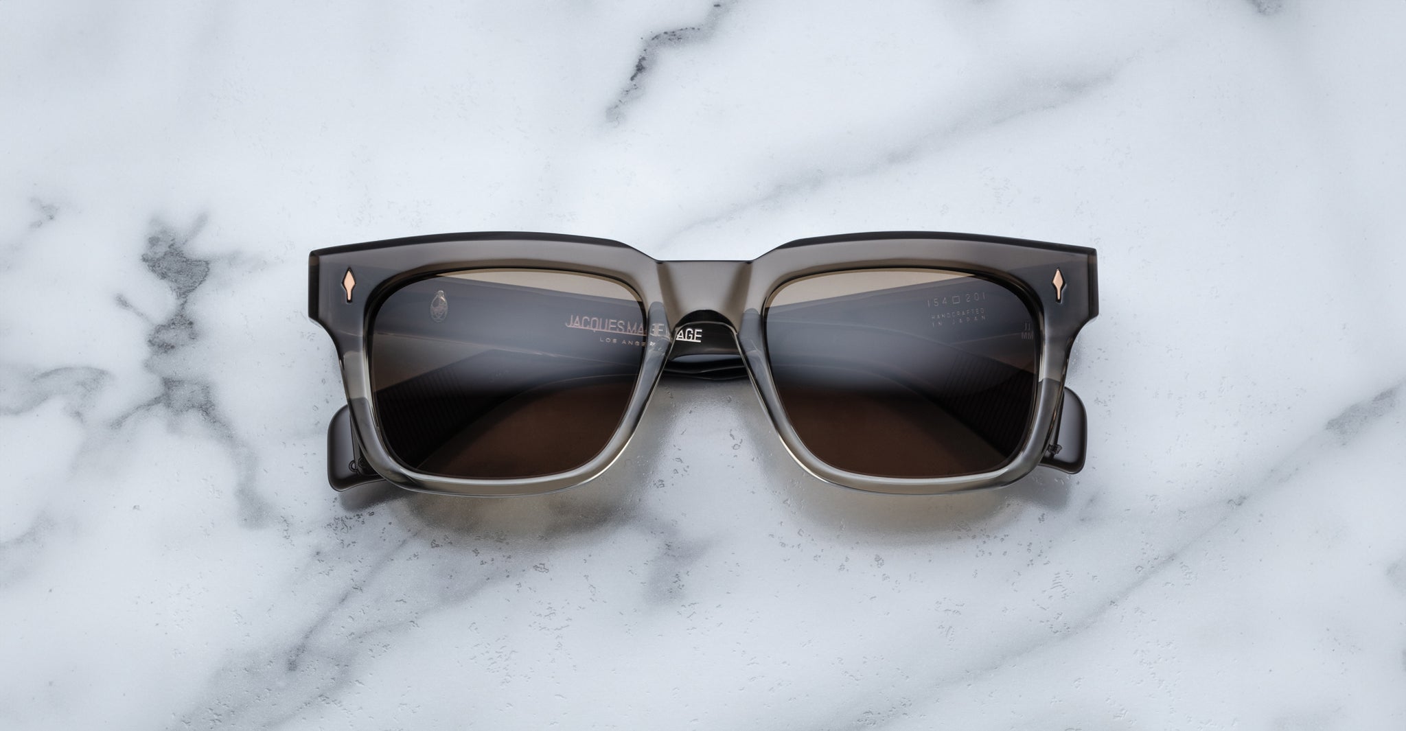 The Jacques Marie Mage Torino, bold rectangular eyeglass frames in dark brown handcrafted acetate by Jacques Marie Mage, rests on a white marble surface.