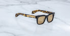 The Jacques Marie Mage Torino sunglasses feature bold rectangular acetate frames, brown tinted lenses, and tortoiseshell-patterned arms, handcrafted by Jacques Marie Mage and displayed on a white marble surface.