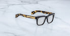 The Jacques Marie Mage Torino eyeglass frames feature bold rectangular black fronts and tortoiseshell-patterned arms, displayed on a white marble surface.