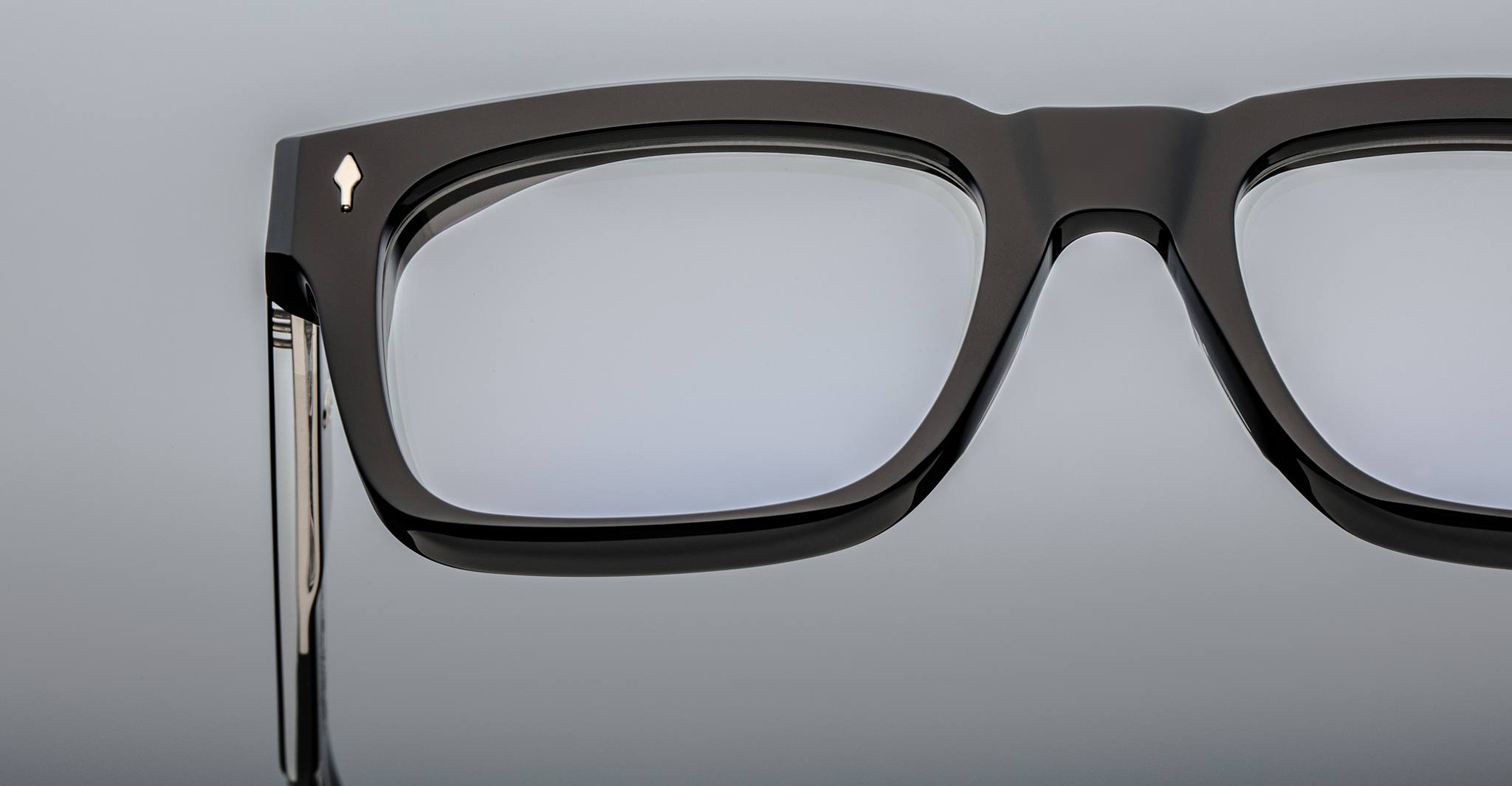 Close-up of the upper left section of bold rectangular Jacques Marie Mage Torino eyewear, handcrafted from acetate, featuring a metallic arrow detail near the hinge.