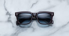 The Jacques Marie Mage Torino sunglasses by Jacques Marie Mage feature bold black rectangular frames and dark lenses, elegantly displayed on a white marble surface.