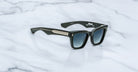 A pair of Jacques Marie Mage Torrance black square sunglasses, from The Shining Collection, featuring limited-edition rectangular frames with dark gradient lenses and metallic temple detailing, resting on a white marble surface.