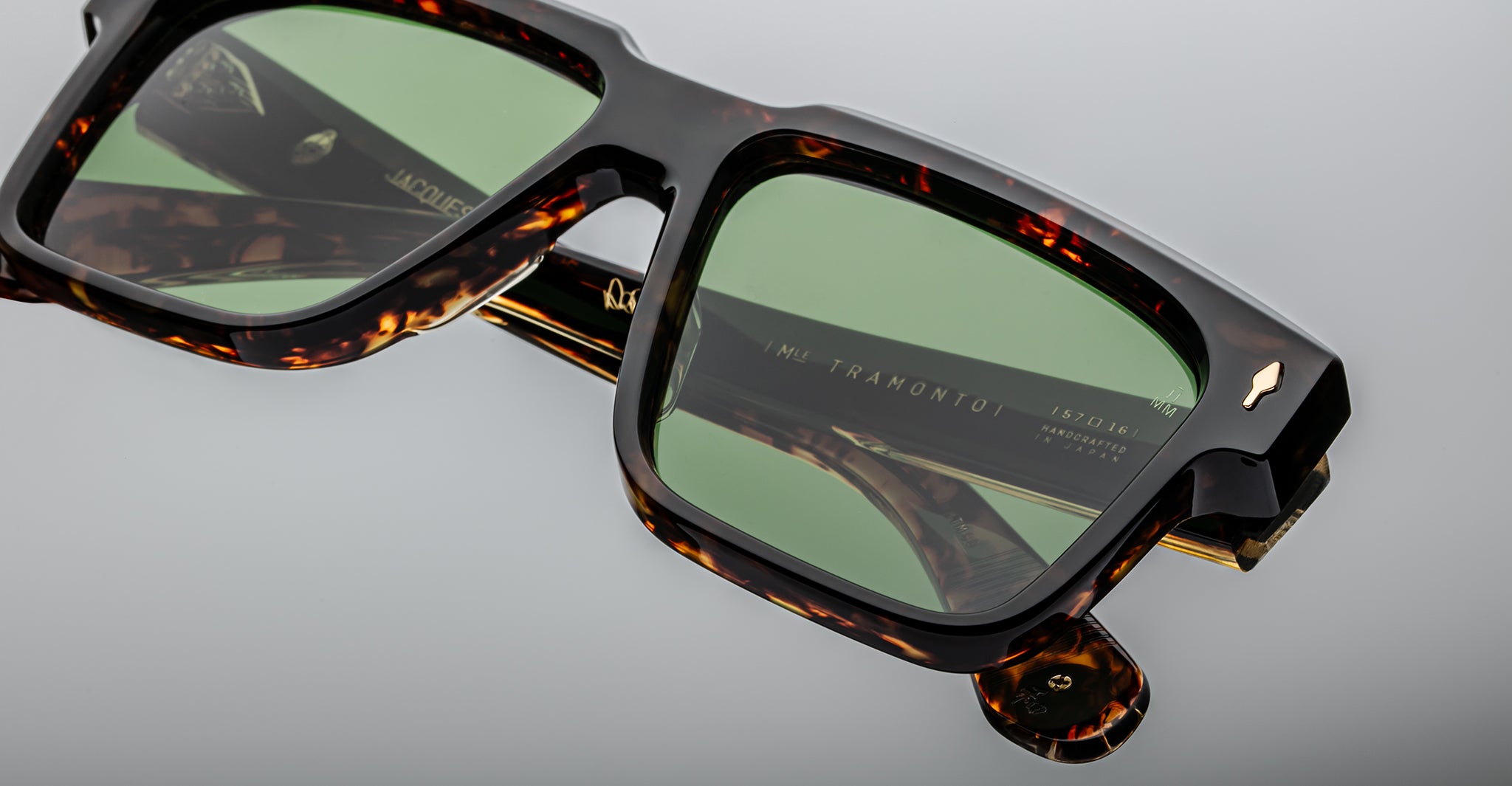 Close-up of stylish tortoiseshell sunglasses with green lenses, showing detailed texture on the frame and a reflection of the brand name TRAMONTO on the inside of the arm.