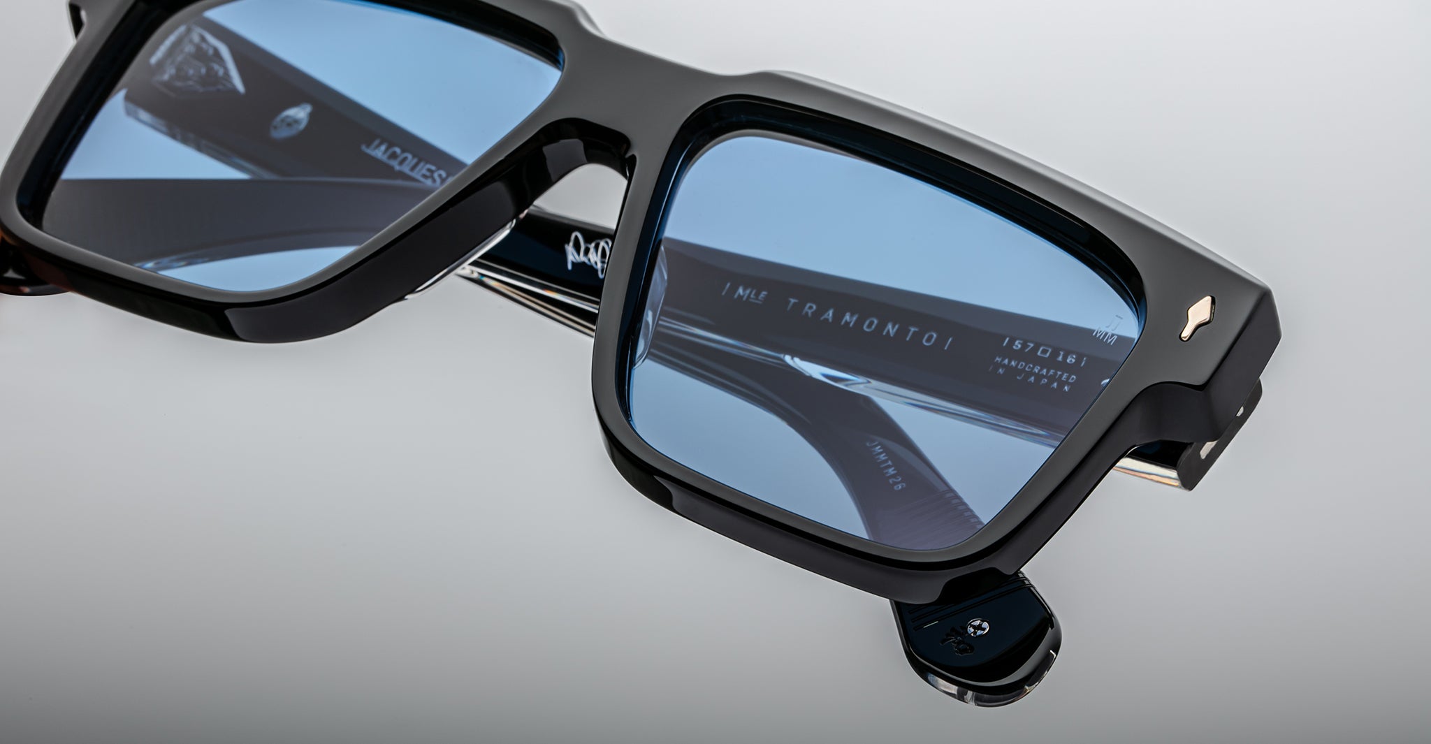 Close-up of stylish black sunglasses with blue-tinted lenses, reflecting text and featuring metallic accents on the temples and hinges, set against a plain light background.