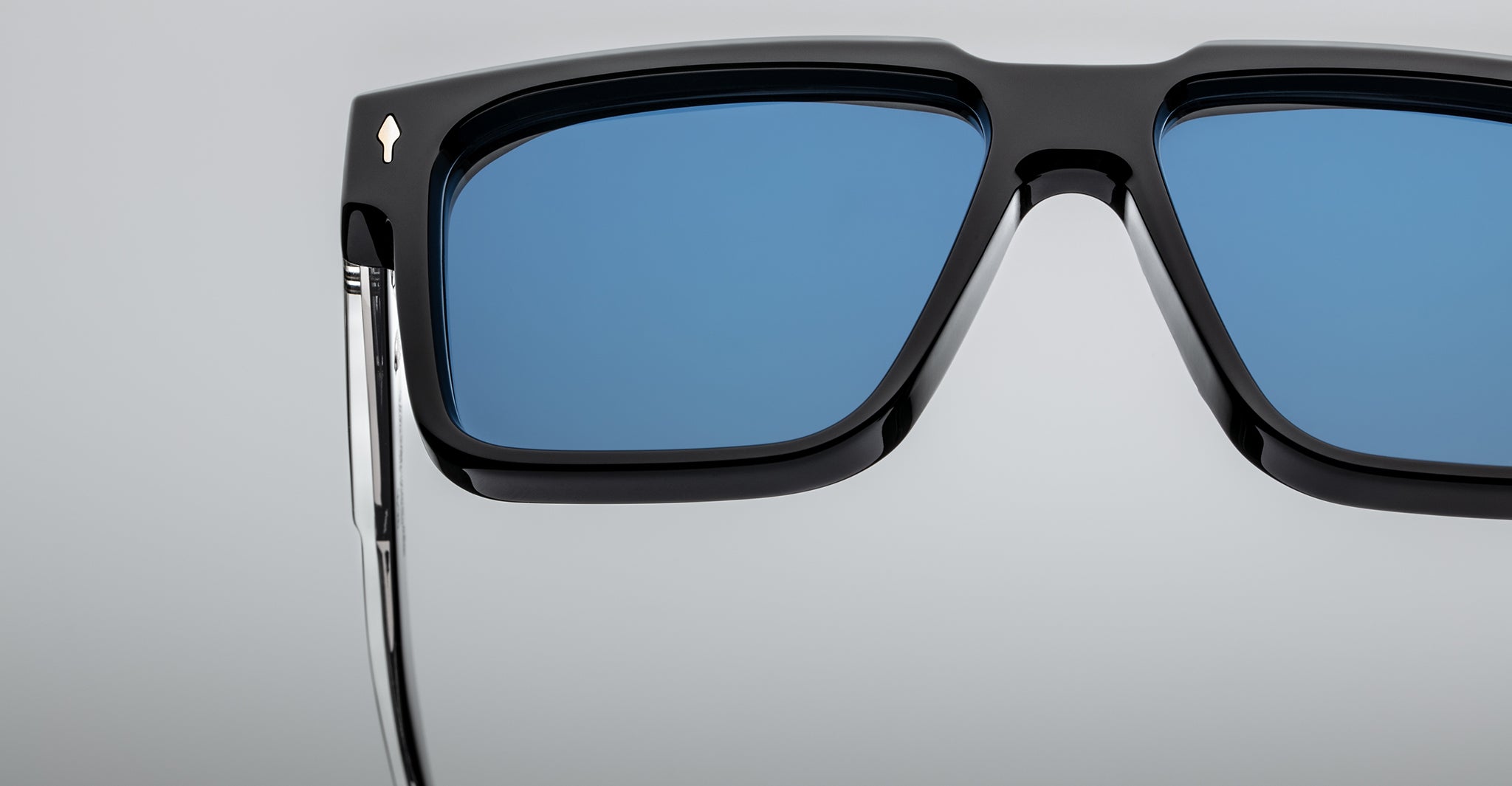Close-up of stylish black sunglasses with blue-tinted rectangular lenses, showing detailed hinges and part of the frame against a light gray background.