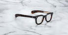 A pair of Jacques Marie Mage Vendome optical frames, featuring a dark tortoiseshell finish and thick design, rests on white marble. Handcrafted in Japan by Jacques Marie Mage.