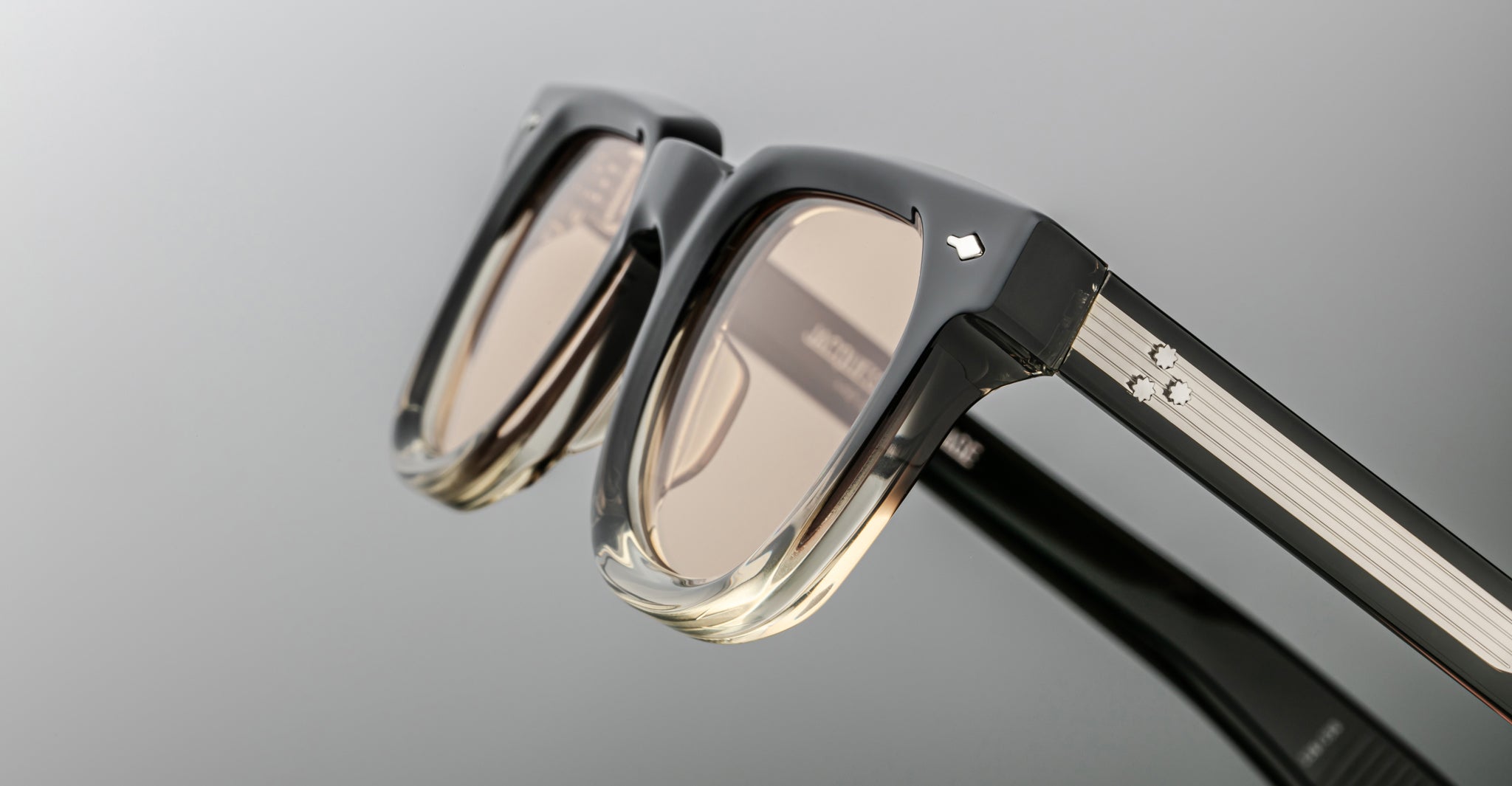 Close-up of Jacques Marie Mage Vendome sunglasses in black and clear acetate, featuring light brown lenses, metallic accents, a subtle temple logo, and expert Japanese craftsmanship.