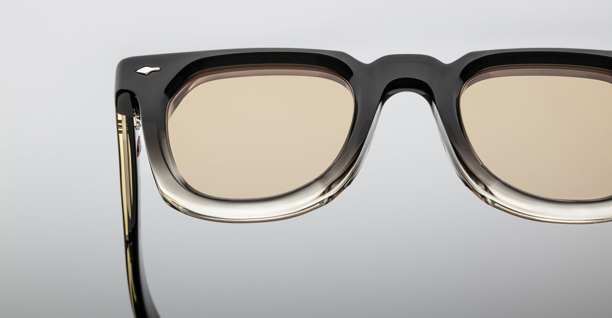 Close-up of Jacques Marie Mage Vendome by Jacques Marie Mage, handcrafted in Japan, showcasing thick black and clear acetate frames with light brown tinted lenses against a neutral background.