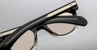 Close-up of Jacques Marie Mage Vendome sunglasses in black with beige-tinted lenses and silver arm details, handcrafted in Japan, shown folded against a light background.