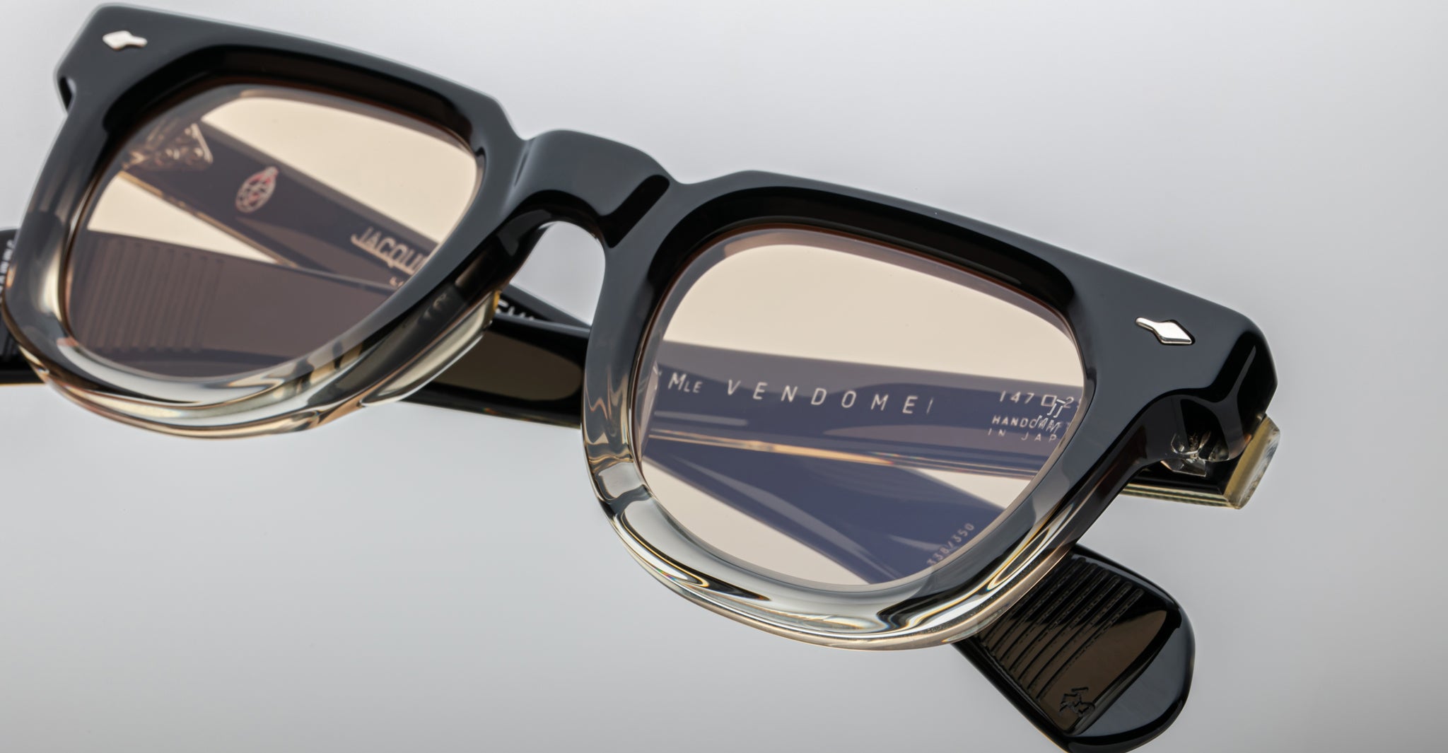 Close-up of Jacques Marie Mage Vendome optical frames, handcrafted in Japan, featuring black rectangular eyeglasses with clear lower rims, brown-tinted lenses, and the “Vendome” name on the inside left temple.