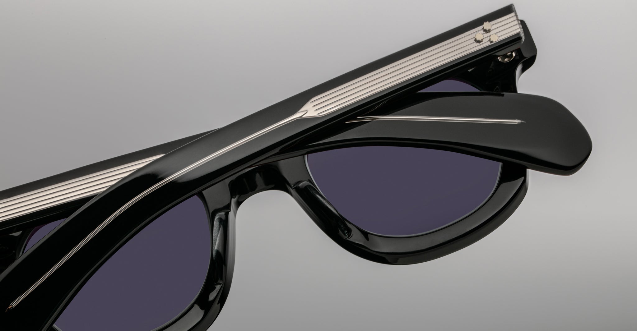 Close-up of Jacques Marie Mage Vendome sunglasses by Jacques Marie Mage, featuring black frames with silver temple detailing, handcrafted in Japan, displayed on a plain grey background.