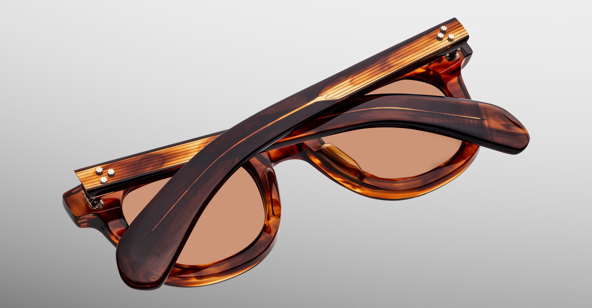 The Jacques Marie Mage Vendome sunglasses by Jacques Marie Mage, in brown tortoiseshell with tinted lenses, are handcrafted in Japan and shown folded on a light gray background.