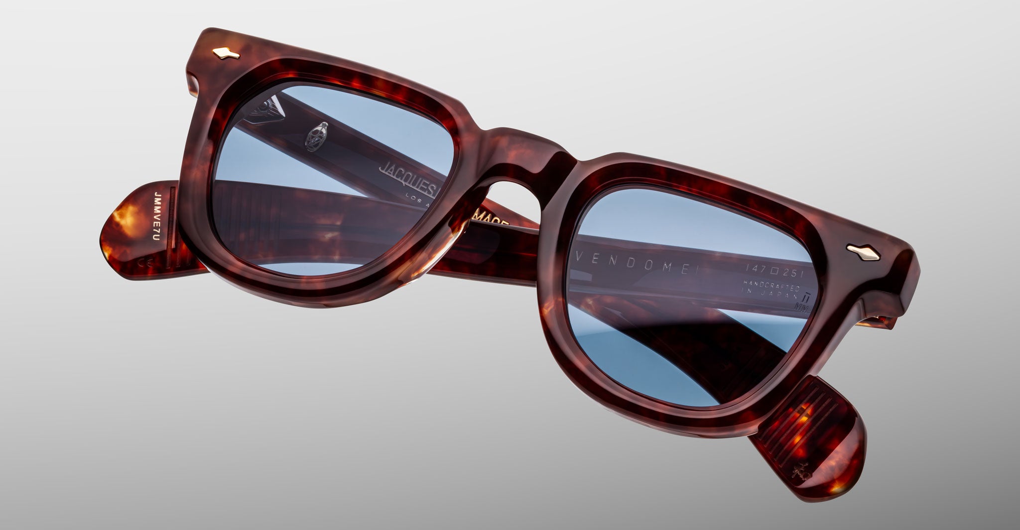 Close-up of Jacques Marie Mage Vendome sunglasses by Jacques Marie Mage, featuring brown tortoiseshell square frames with blue-tinted lenses, handcrafted in Japan, set against a plain light gray background.