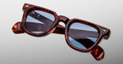 Close-up of Jacques Marie Mage Vendome sunglasses by Jacques Marie Mage, featuring brown tortoiseshell square frames with blue-tinted lenses, handcrafted in Japan, set against a plain light gray background.