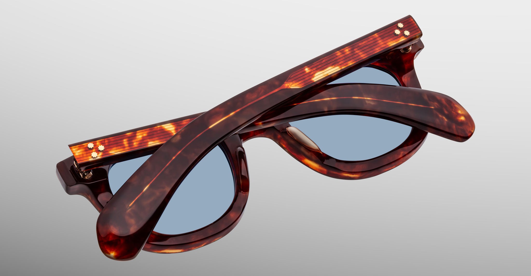 Jacques Marie Mage Vendome sunglasses, featuring tortoiseshell frames and blue lenses, are expertly handcrafted in Japan and shown folded on a gray gradient background.