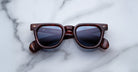 Jacques Marie Mage Vendome sunglasses by Jacques Marie Mage, featuring brown tortoiseshell square frames and dark lenses, handcrafted in Japan, displayed on a white marble surface.