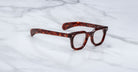 A pair of Jacques Marie Mage Vendome optical frames by Jacques Marie Mage, featuring a thick tortoiseshell design and clear lenses, rests on a white marble surface.