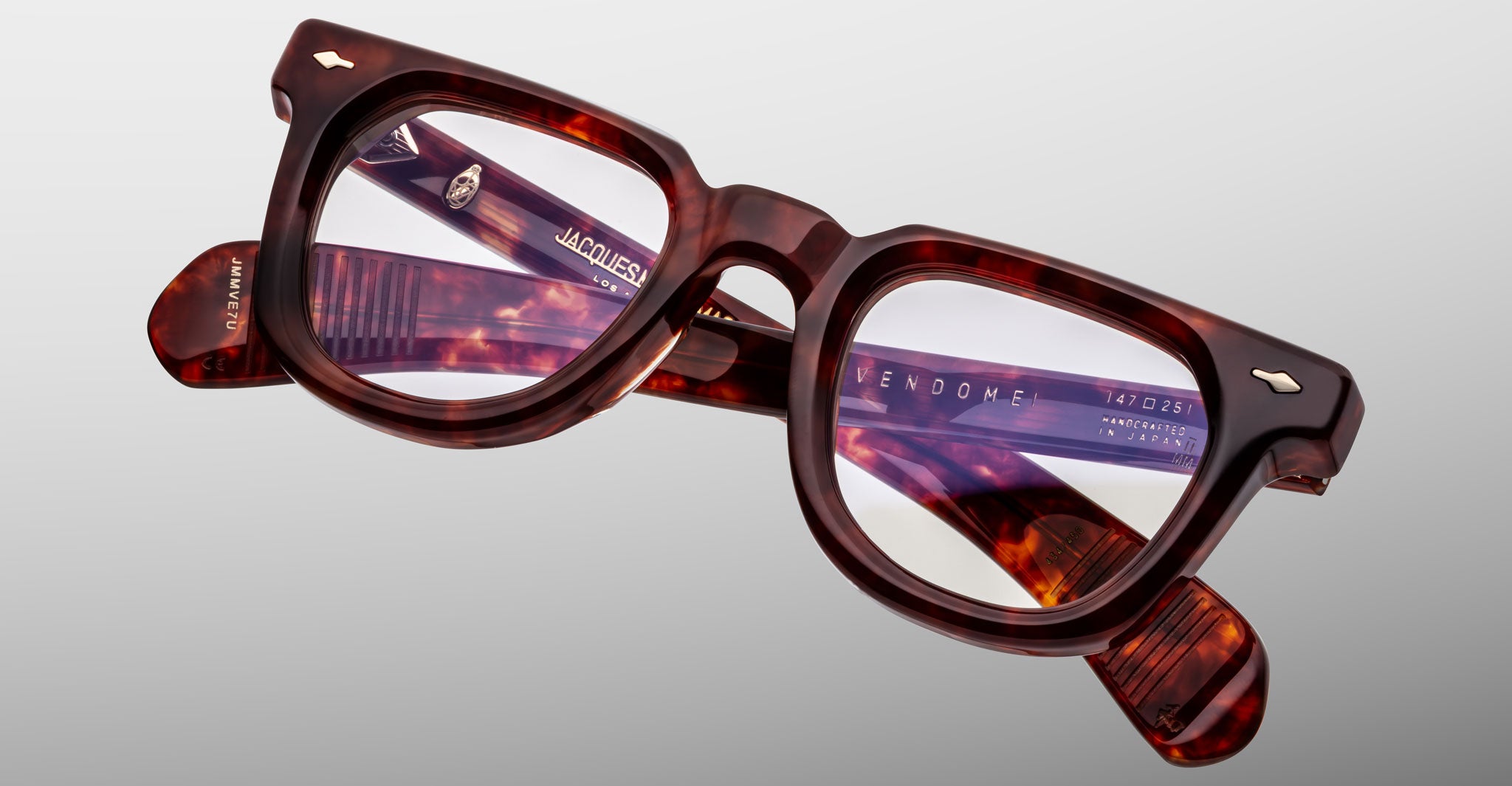 Close-up of Jacques Marie Mage Vendome optical frames, handcrafted tortoiseshell rectangular eyeglasses by Jacques Marie Mage with model details engraved on the inner arms, shown against a light gray background.