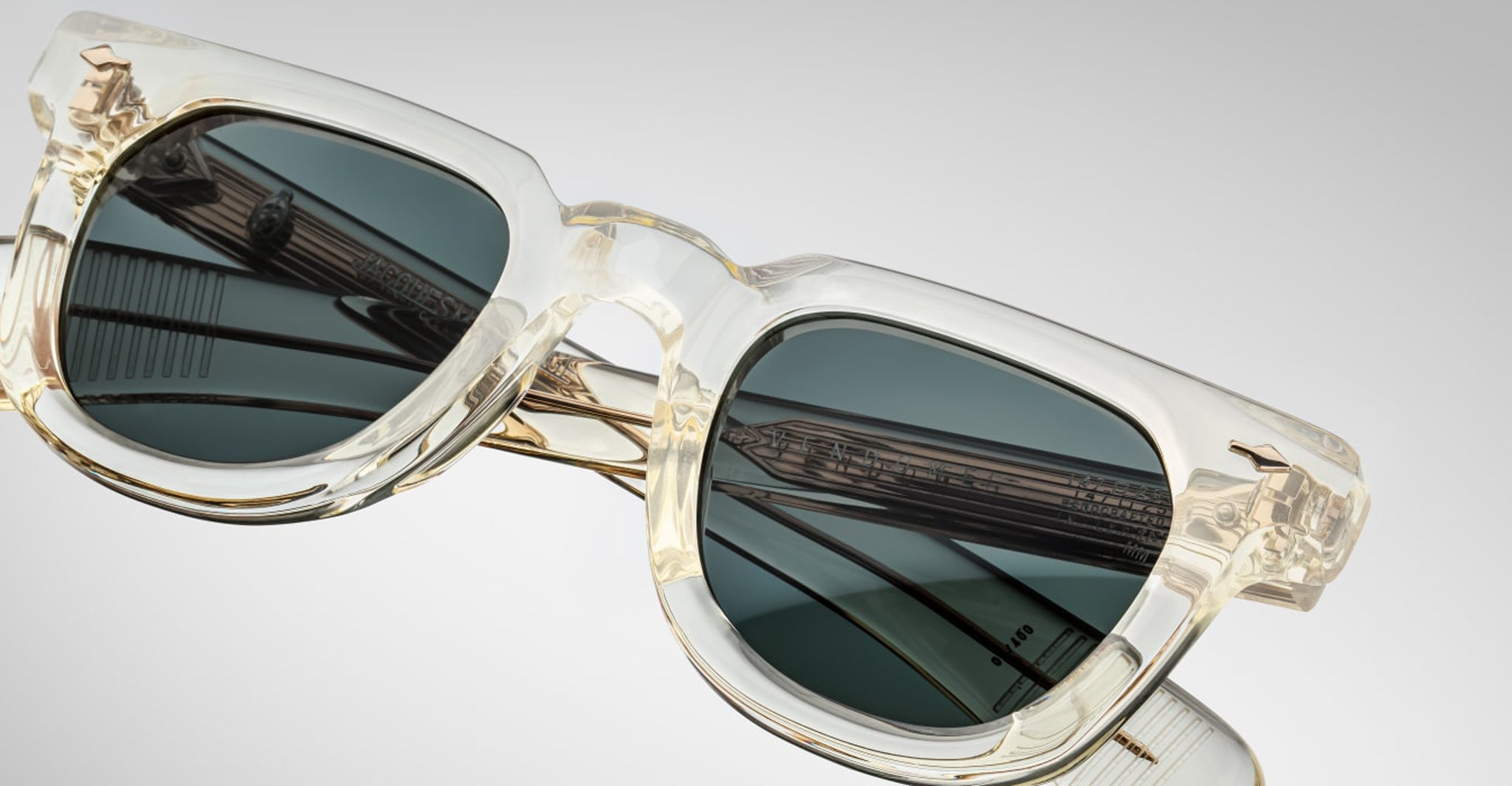 Close-up of Jacques Marie Mage Vendome sunglasses by Jacques Marie Mage, featuring transparent frames, dark lenses, and metal arms—handcrafted in Japan—set against a plain light background.