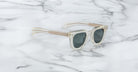 Jacques Marie Mage Vendome sunglasses with clear frames, dark lenses, and gold-tone temples by Jacques Marie Mage are displayed on a white marble surface.