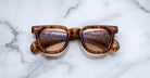 Jacques Marie Mage Vendome sunglasses by Jacques Marie Mage, featuring brown tortoiseshell rectangular frames, handcrafted in Japan, elegantly displayed on a white marble surface.