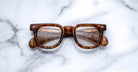 Jacques Marie Mage Vendome optical frames by Jacques Marie Mage, featuring thick brown tortoiseshell edges and handcrafted in Japan, are displayed on a white marble surface and viewed from above.