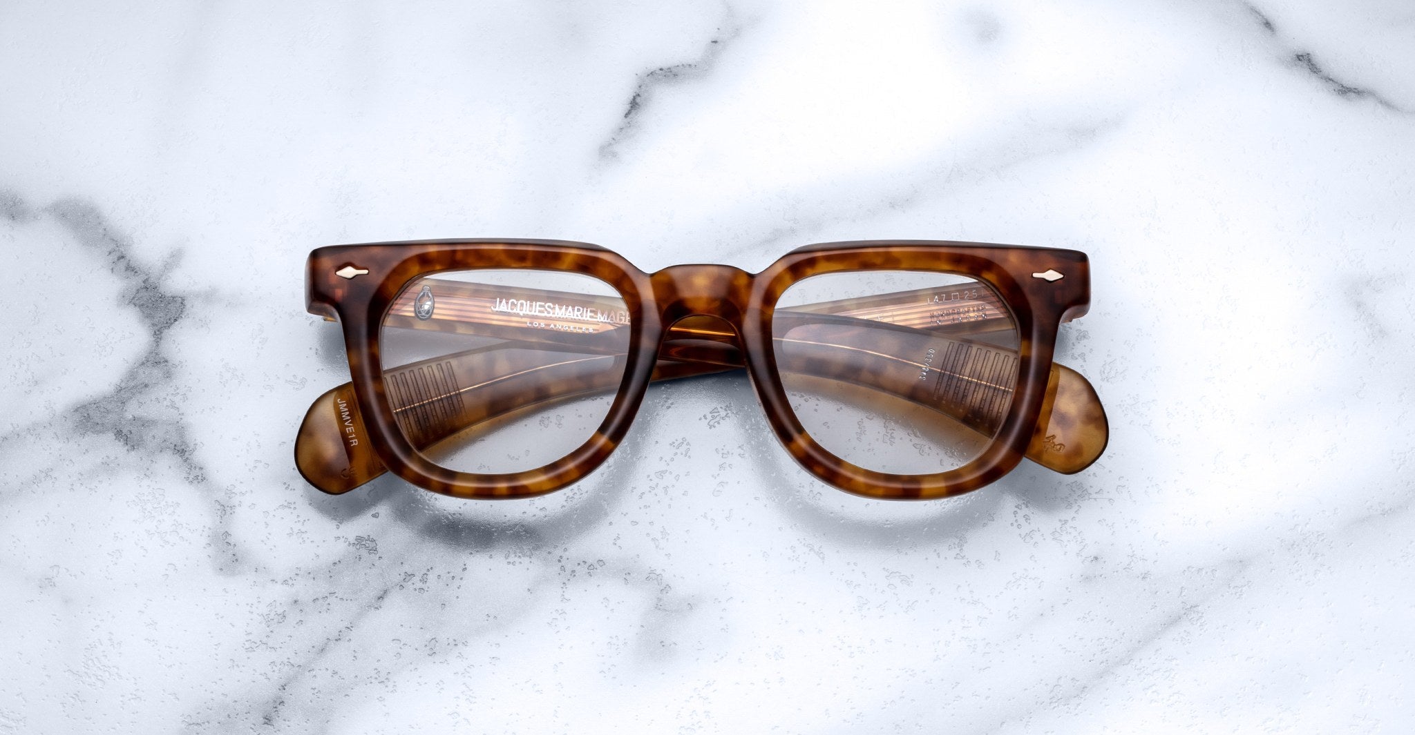 Jacques Marie Mage Vendome optical frames by Jacques Marie Mage, featuring thick brown tortoiseshell edges and handcrafted in Japan, are displayed on a white marble surface and viewed from above.