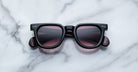 Jacques Marie Mage Vendome black square sunglasses with dark lenses, handcrafted in Japan, rest on a white marble surface.