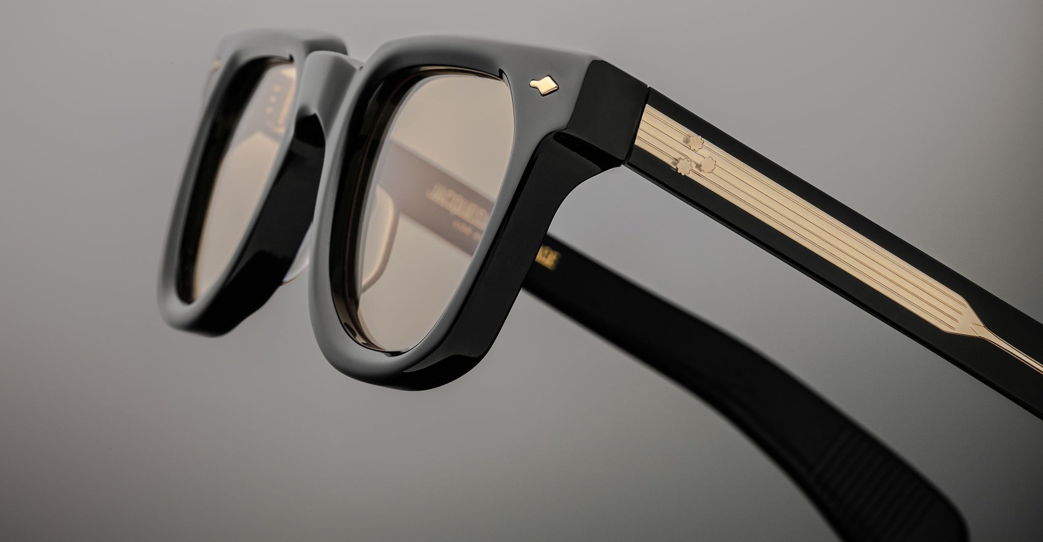 Close-up of Jacques Marie Mage Vendome sunglasses, featuring black frames and gold-detailed arms, handcrafted in Japan, displayed on a plain gray background.
