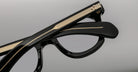 Close-up of Jacques Marie Mage Vendome eyeglasses by Jacques Marie Mage, handcrafted in Japan, featuring black frames with gold arm detailing and one arm folded over the front.