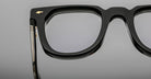 Close-up of the upper half of Jacques Marie Mage Vendome optical frames in black, handcrafted in Japan, with a gold accent by the hinge, shown against a plain gray background.