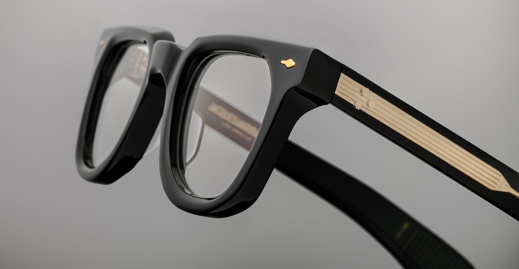 Close-up of Jacques Marie Mage Vendome optical frames by Jacques Marie Mage, handcrafted in Japan with black frames and gold-detailed temples, displayed on a plain grey background.
