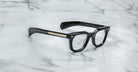 Jacques Marie Mage Vendome black rectangular optical frames with gold arm detailing, handcrafted in Japan, displayed on white marble.