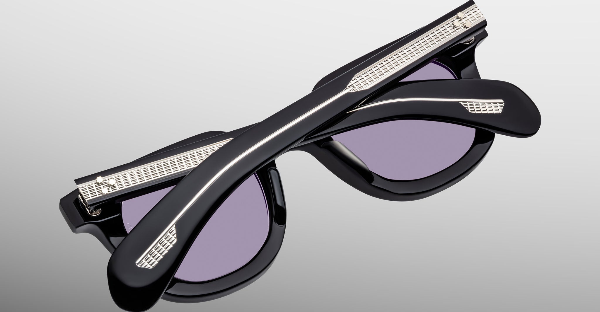 Close-up of Jacques Marie Mage Vendome sunglasses in black with purple lenses, folded on a light gray background—expertly handcrafted in Japan by Jacques Marie Mage.