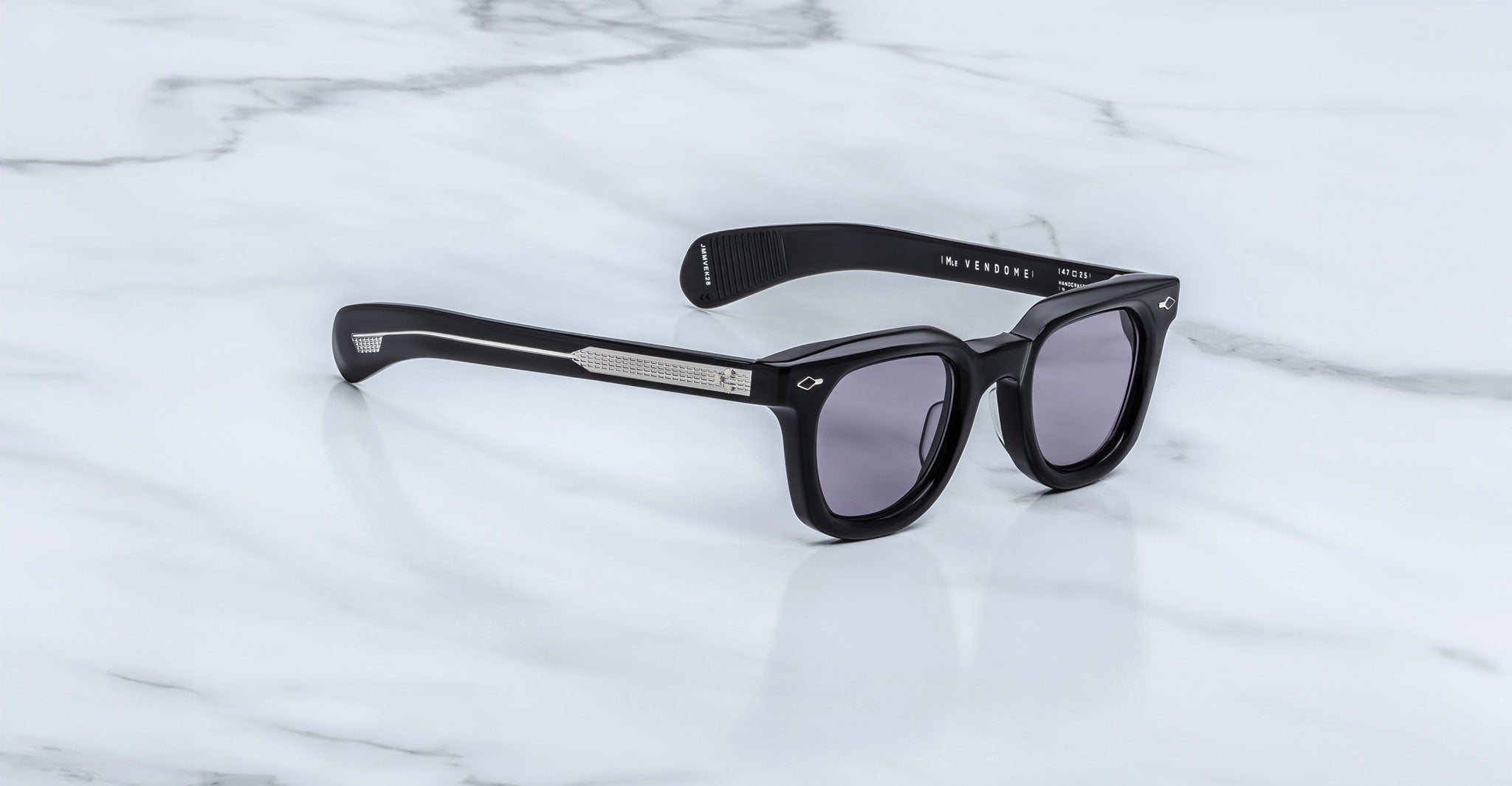The Jacques Marie Mage Vendome sunglasses by Jacques Marie Mage feature black rectangular thick frames with silver temple detailing, handcrafted in Japan, displayed on a white marble surface.