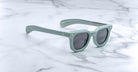Jacques Marie Mage Vendome sunglasses in pale green with dark lenses rest on white marble, showcasing the brand’s expert Japanese handcrafted craftsmanship.