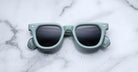 A pair of Jacques Marie Mage Vendome sunglasses in mint green with dark lenses sits atop a white marble surface.